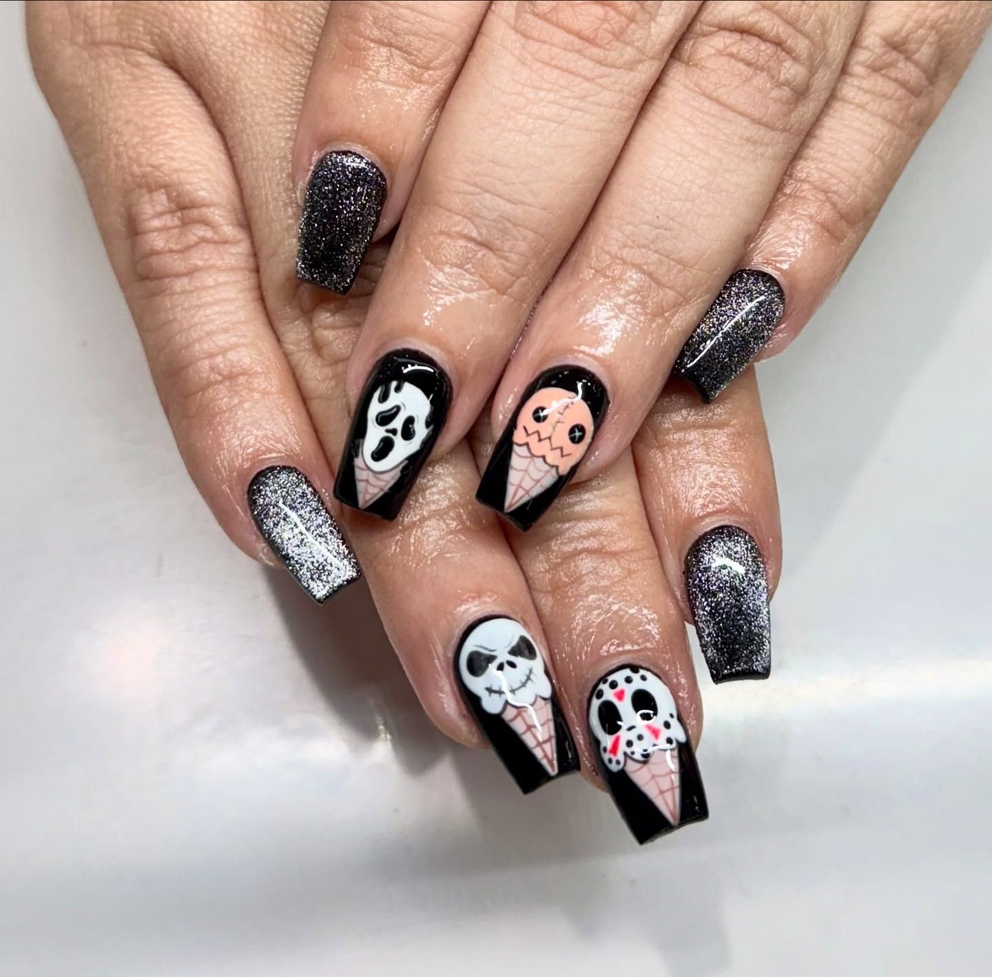 Black glitter nails with Halloween skull nail art in black, white, and peach on a hand