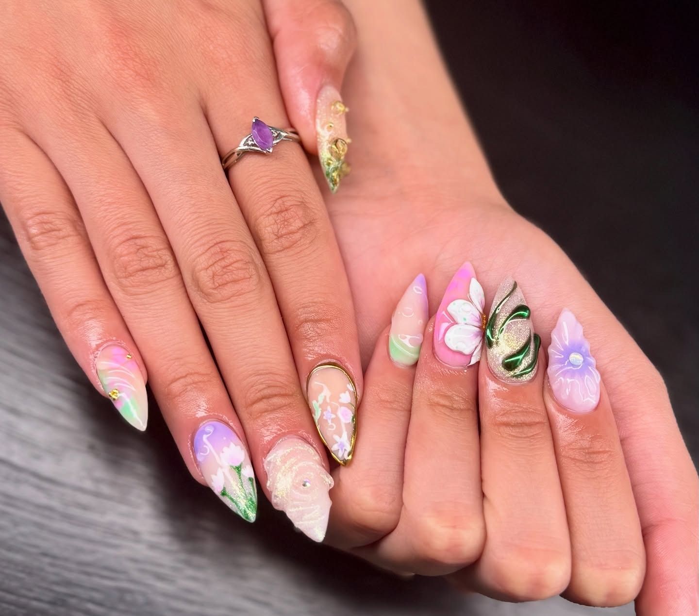 Hands with pastel rainbow and floral nail art, including 3D butterfly and gem accents