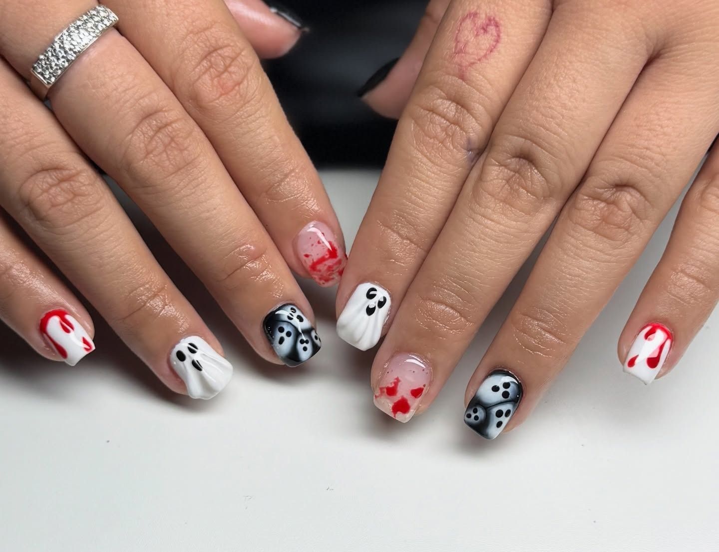 Hands with black, white, and red Halloween-themed nail art and silver rings on a white surface