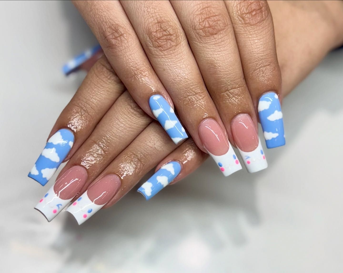 Hands with long pastel blue and white nails, plus pink and white nails with floral accents.
