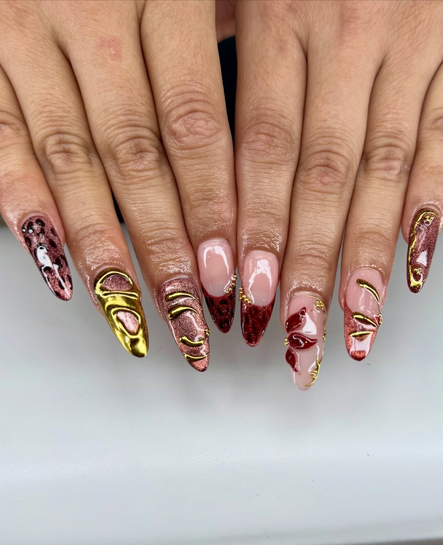 Hands with long, glossy pink, red, gold, and brown patterned nail art on a white background
