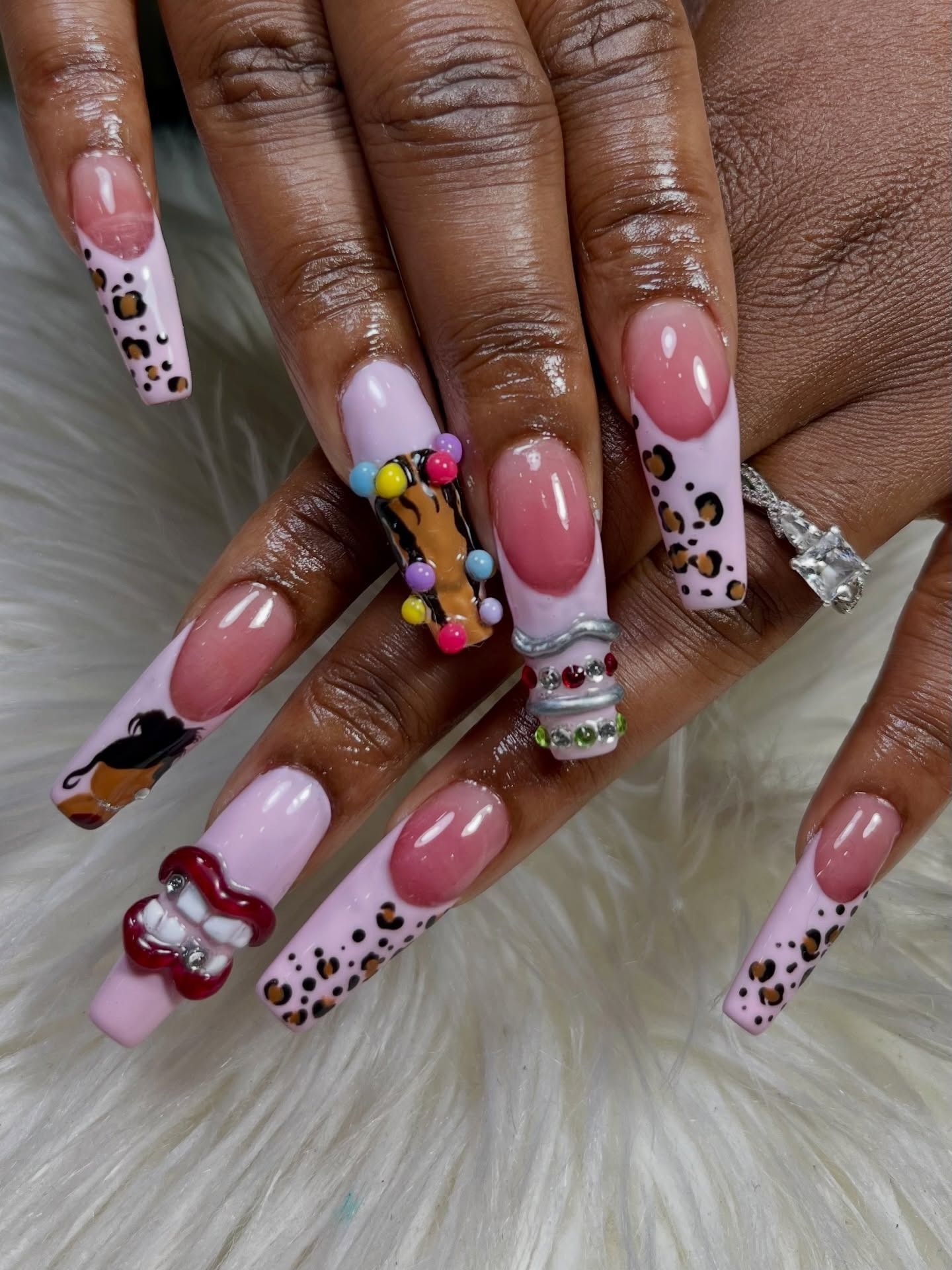 Pink almond nails with white and leopard accents, plus colorful 3D charms on ring fingers.