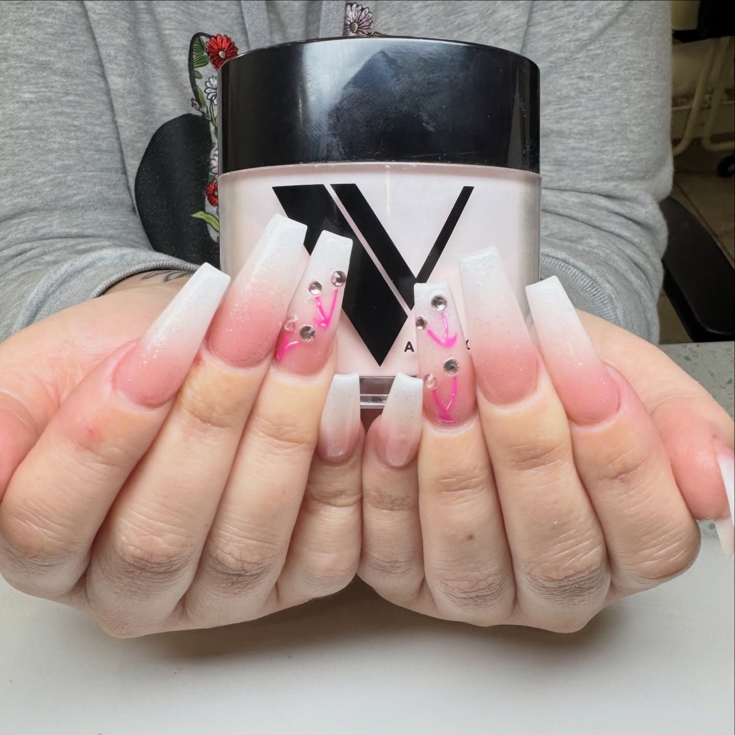 Hands displaying long pink-and-white acrylic nails with black heart designs, holding a black-and-white cup.