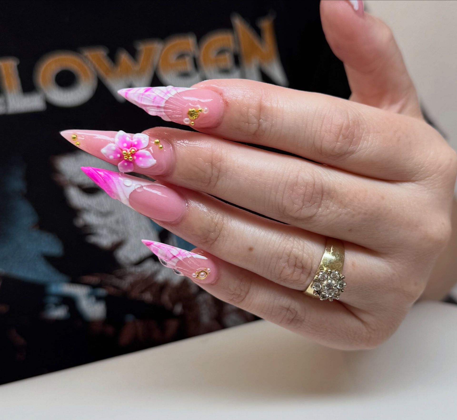 Hand with pink floral acrylic nails and a gold ring resting on a table