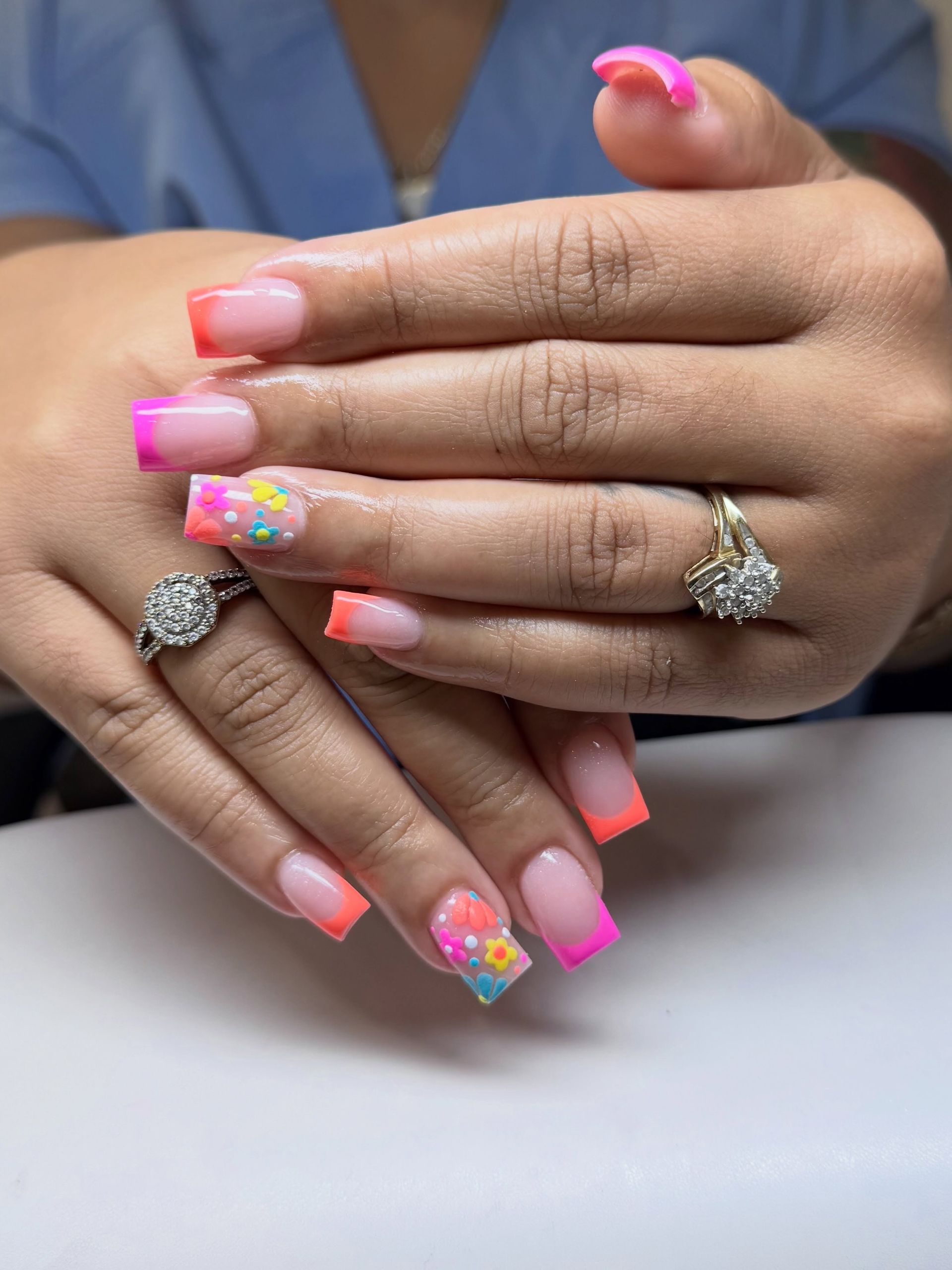 Hands with pink gradient and floral nail art, showing silver rings on a white table.