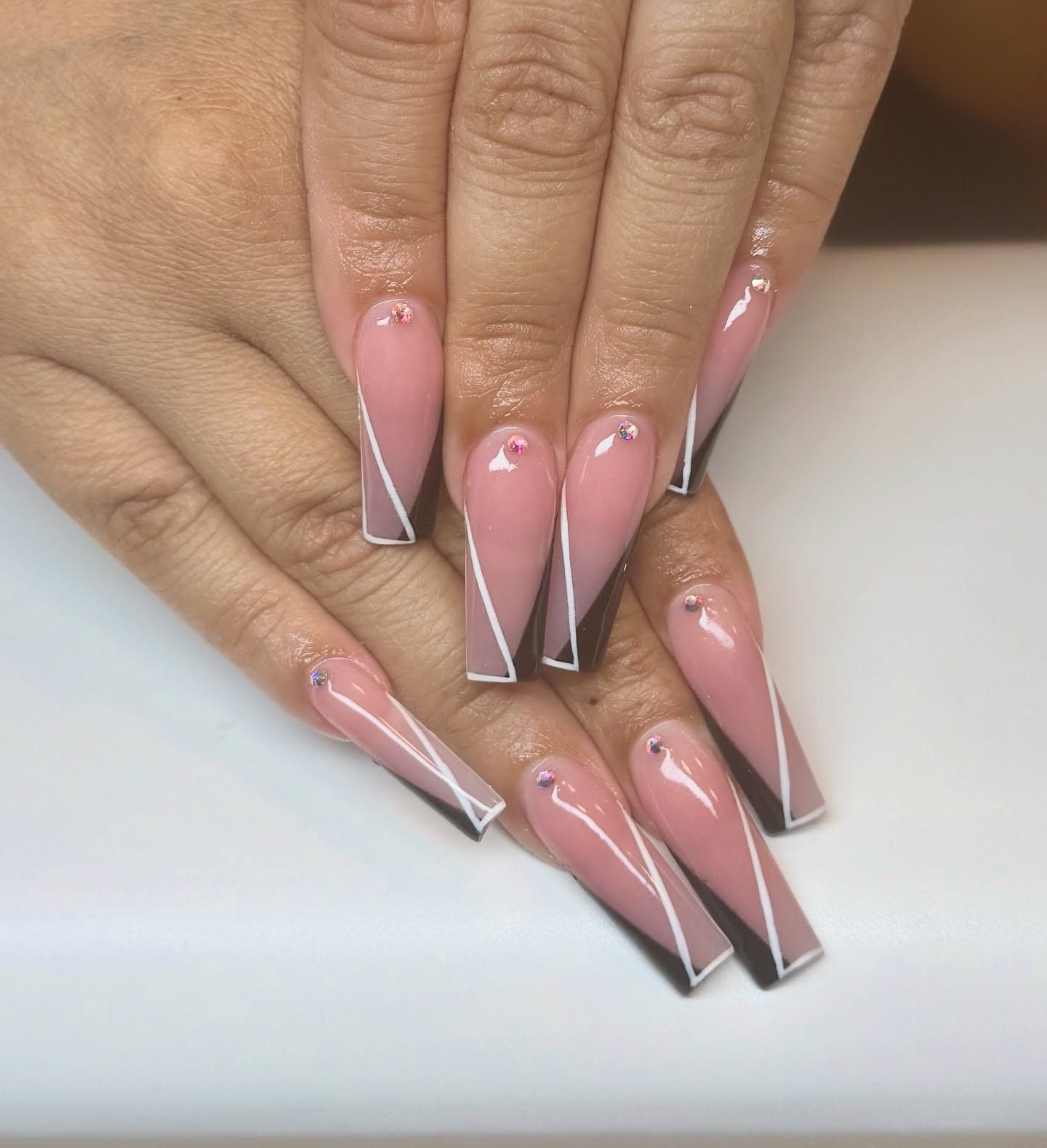 Hands with long pink-and-white stiletto acrylic nails posed on a white surface