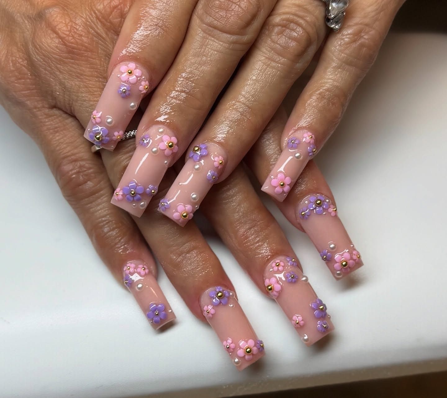 Hands with long pink and lavender floral nail art on a white surface