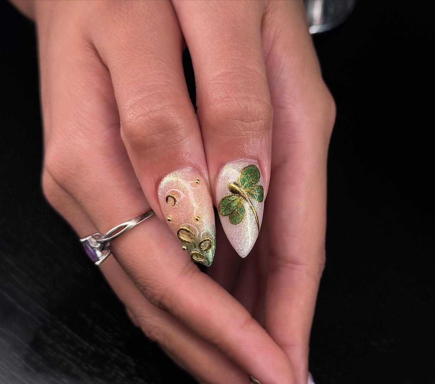 Hand with long white and gold floral nails, wearing a silver ring, on a black background