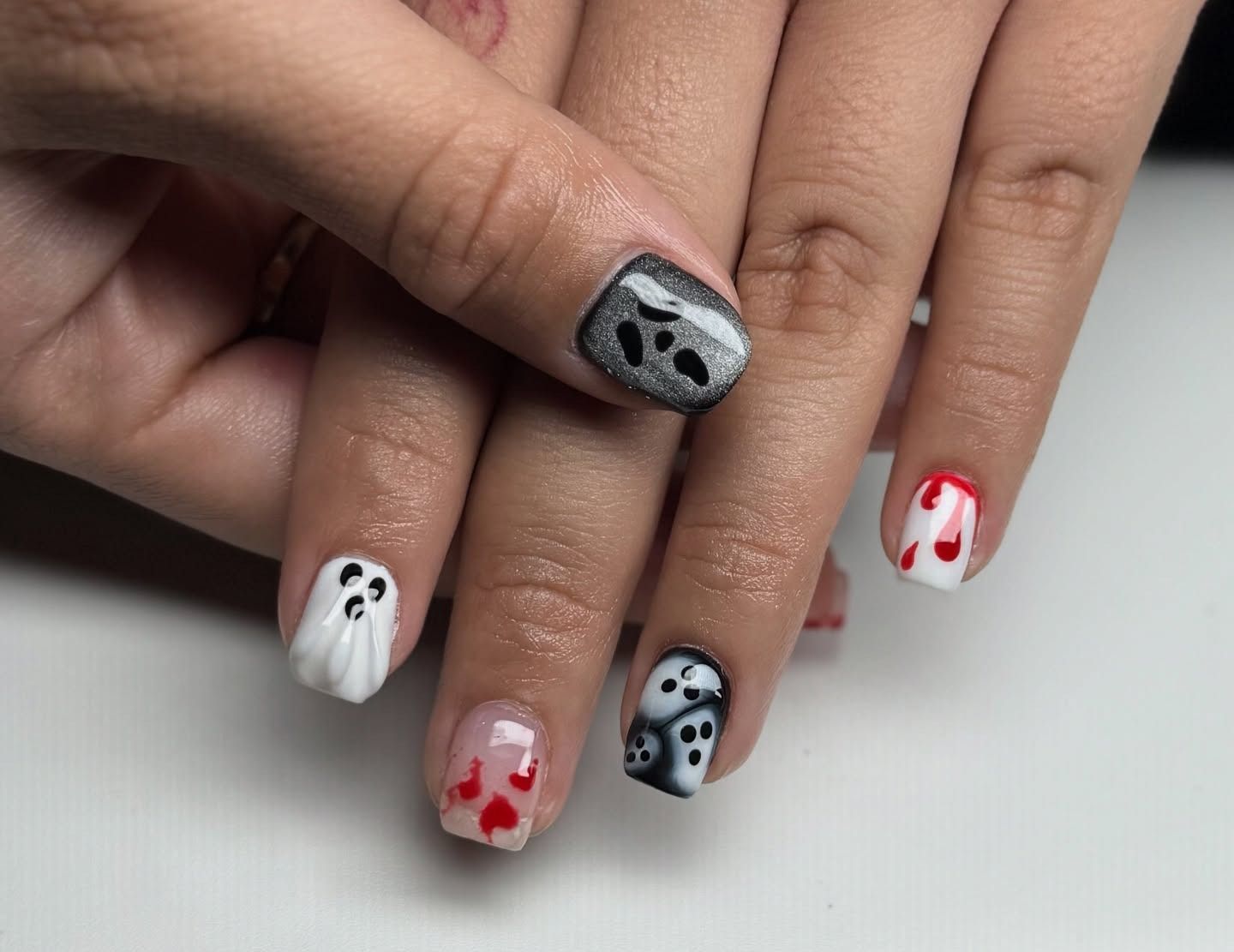 Hands with black, white, and red Halloween-themed nail art, including ghost and face designs.