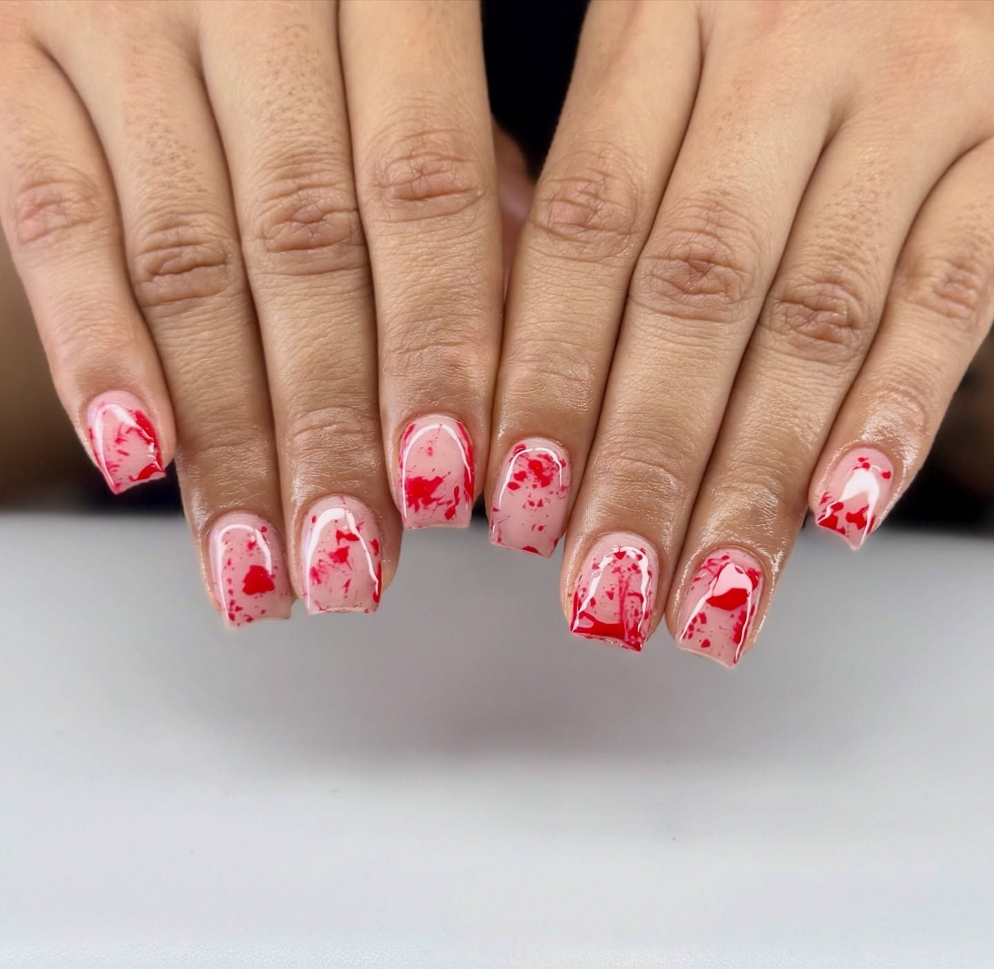 Hands with red and white speckled nail art resting on a white surface