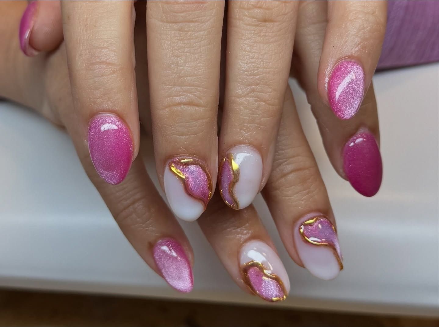 Hand with pink and white glitter manicure and gold swirl accents on long nails