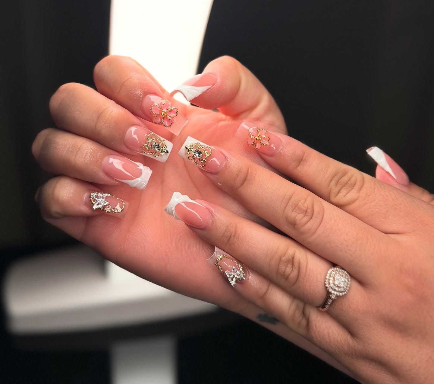 Hands with long pink-and-white floral manicure and a ring, shown close up against a dark background
