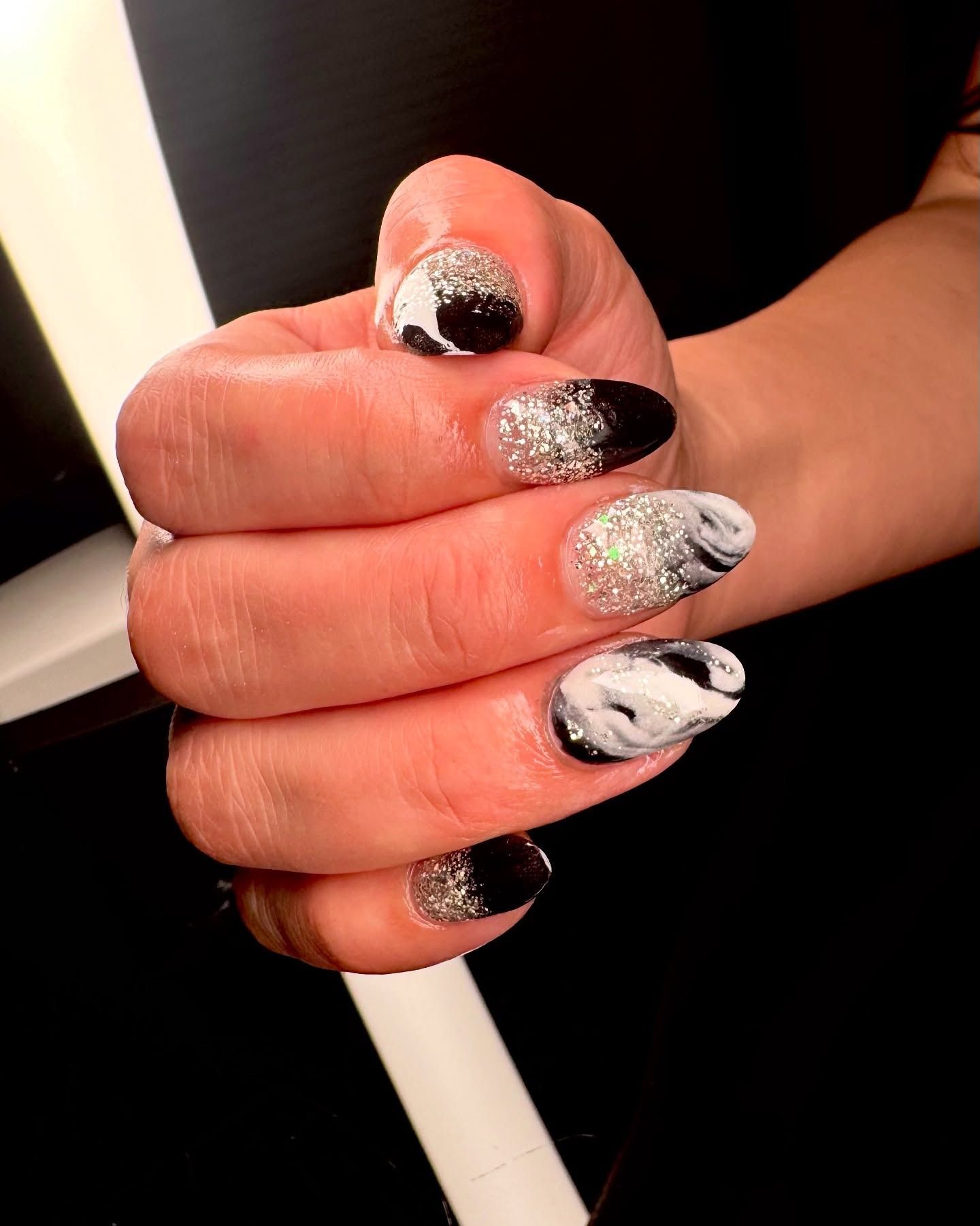 Hand with black, white, and silver glitter nail art gripping a white rod