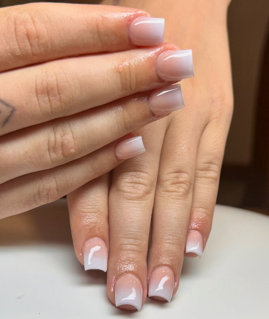 Hands with pale pink French manicure nails overlapped on a soft background.