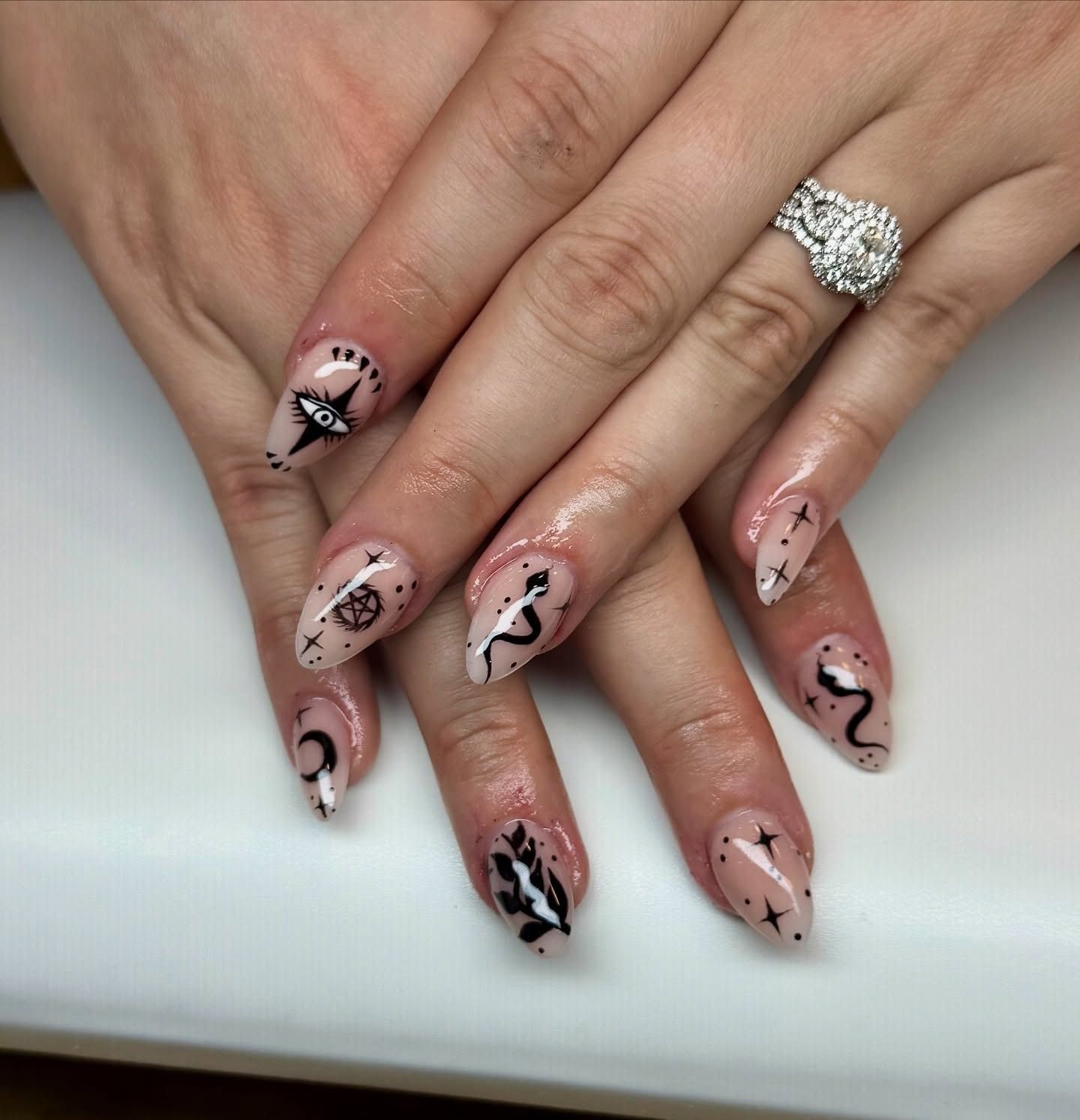 Hands with pink-and-black abstract nail art and a sparkling ring on a white background