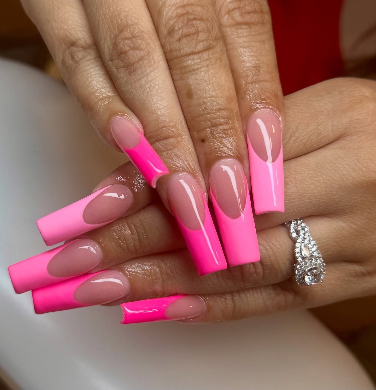Hands with long neon pink French-tip acrylic nails and a silver ring.
