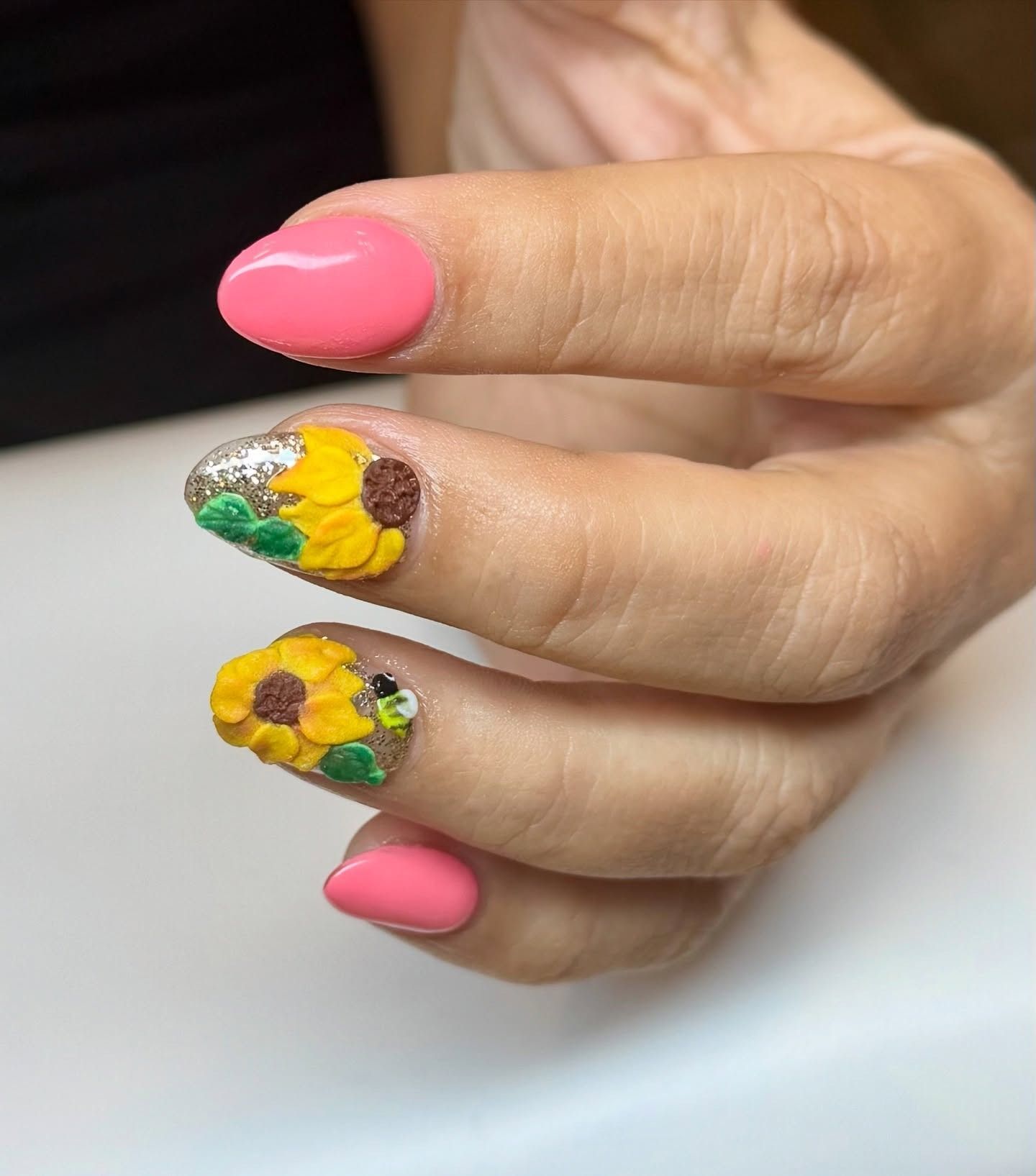 Hand with pink nails and two sunflower nail art designs on a white background