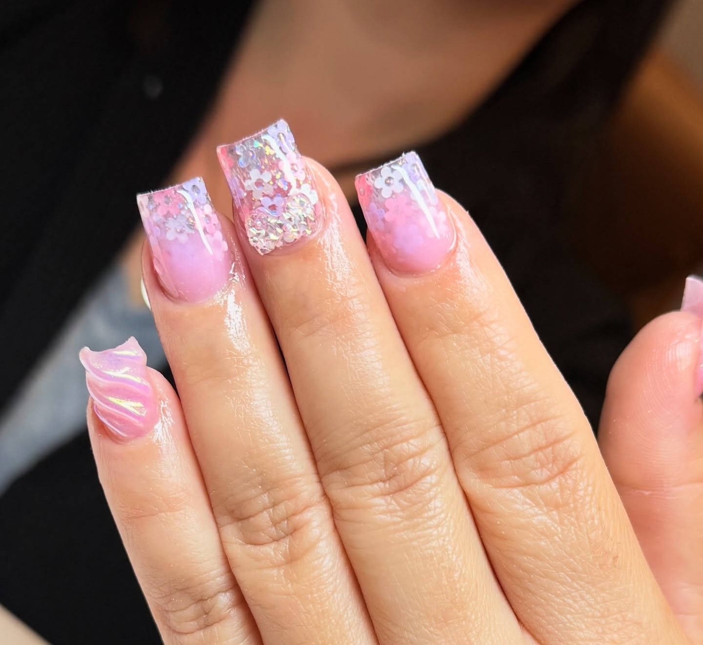 Hand with pink glitter acrylic nails and floral accents, shown in close-up.
