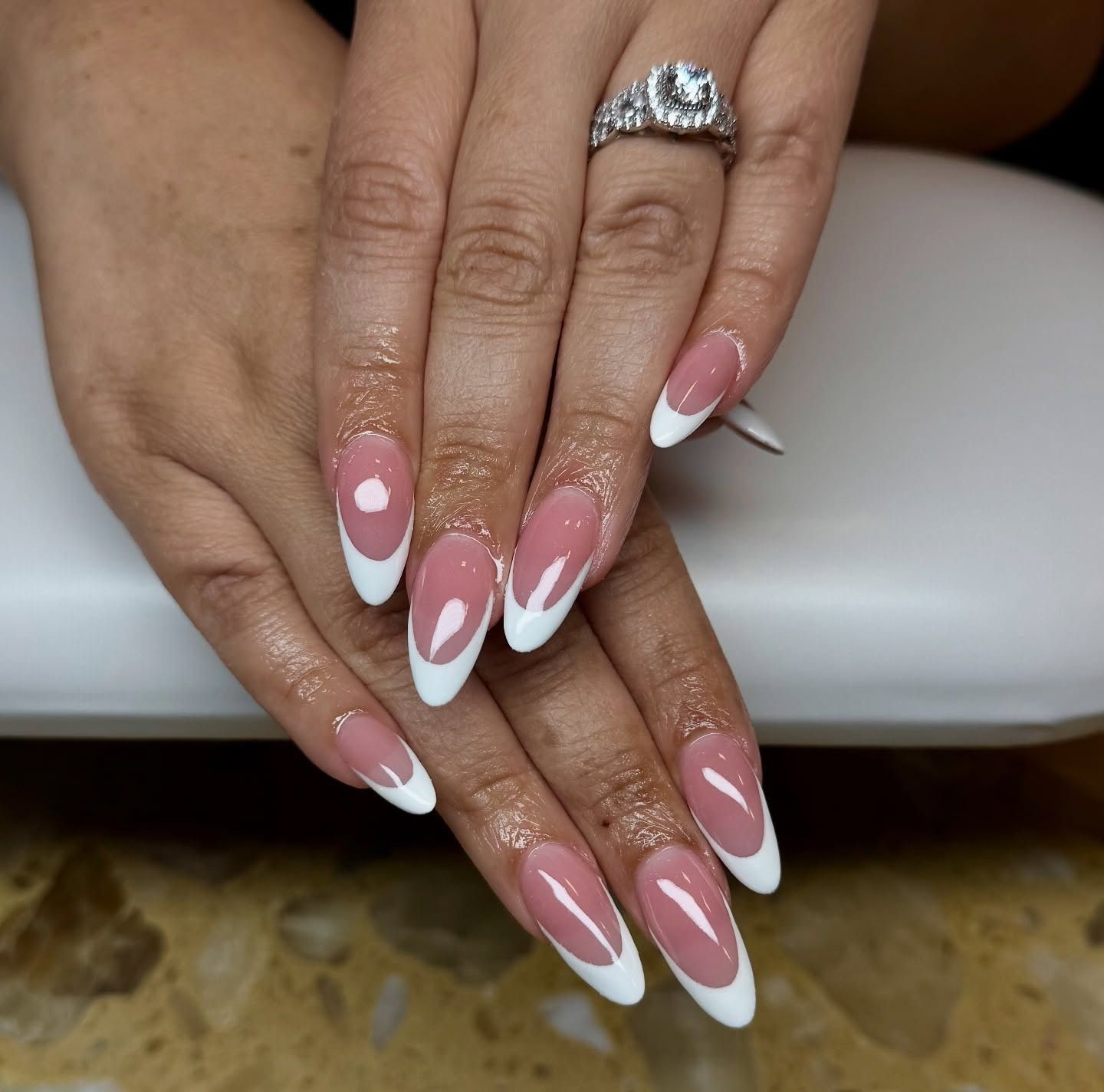 Hands with pink-and-white French tip nails and a silver ring resting on a chair arm.