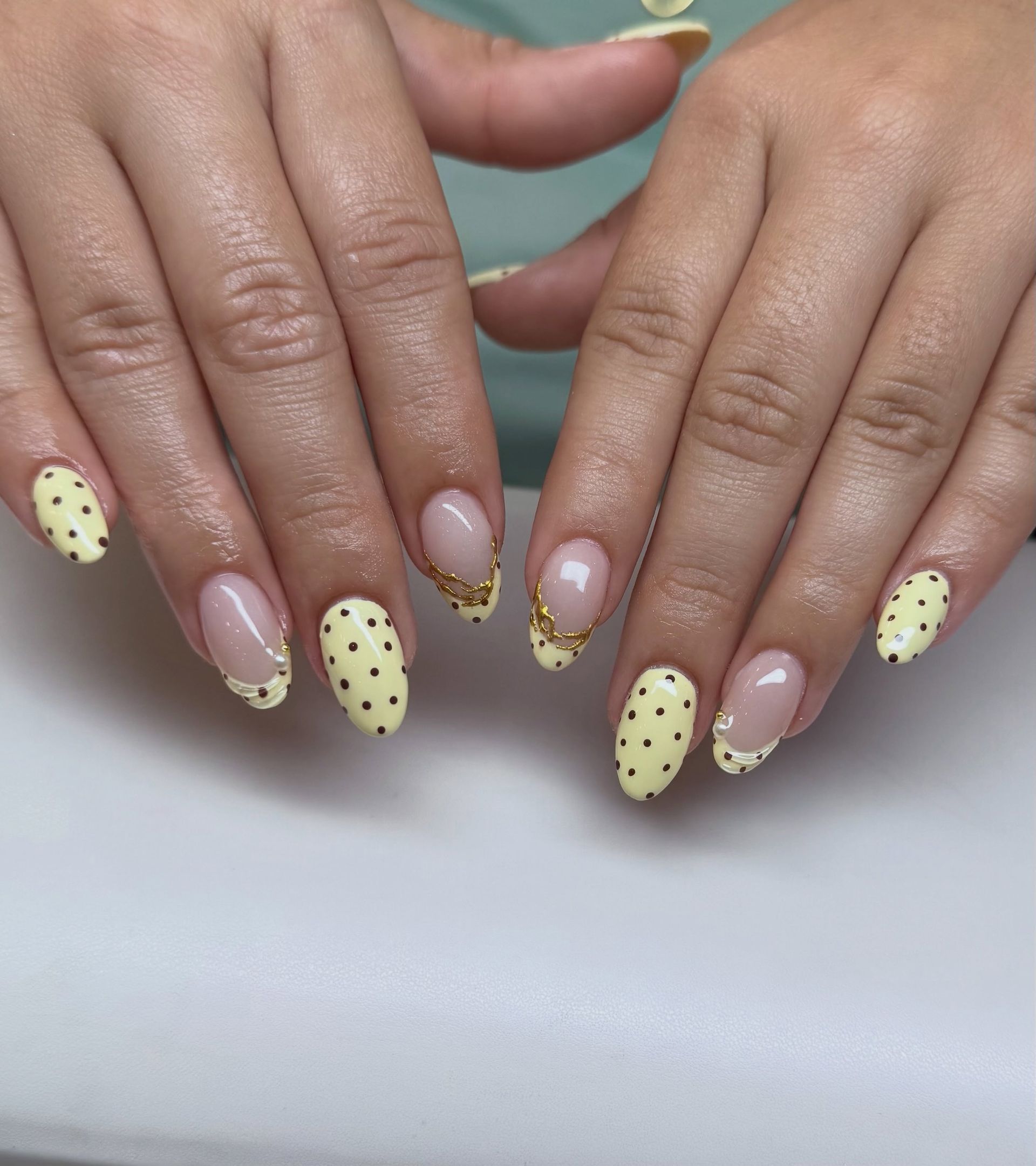 Hands with pale yellow polka-dot manicure on a white background