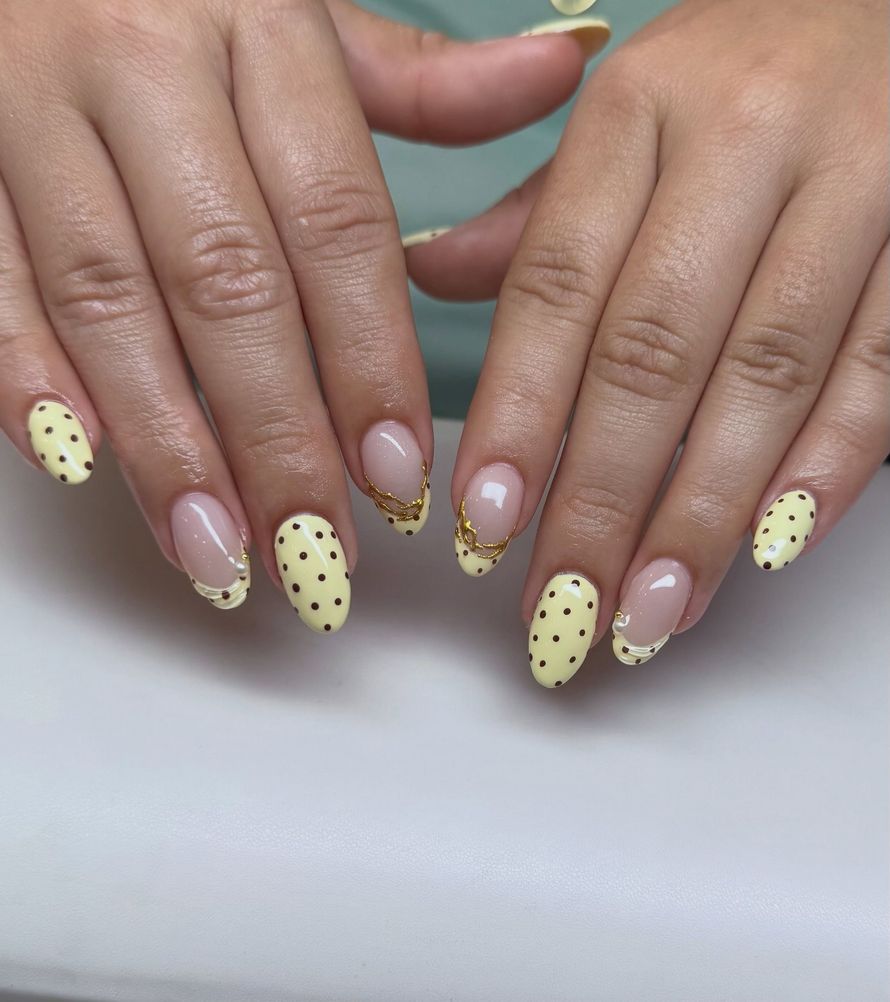 Hands with pale yellow polka-dot and nude manicured nails on a white background