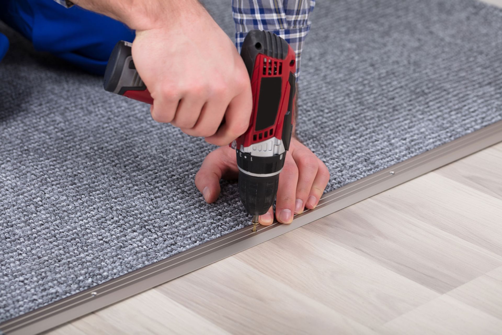 A man is installing a carpet with a drill.