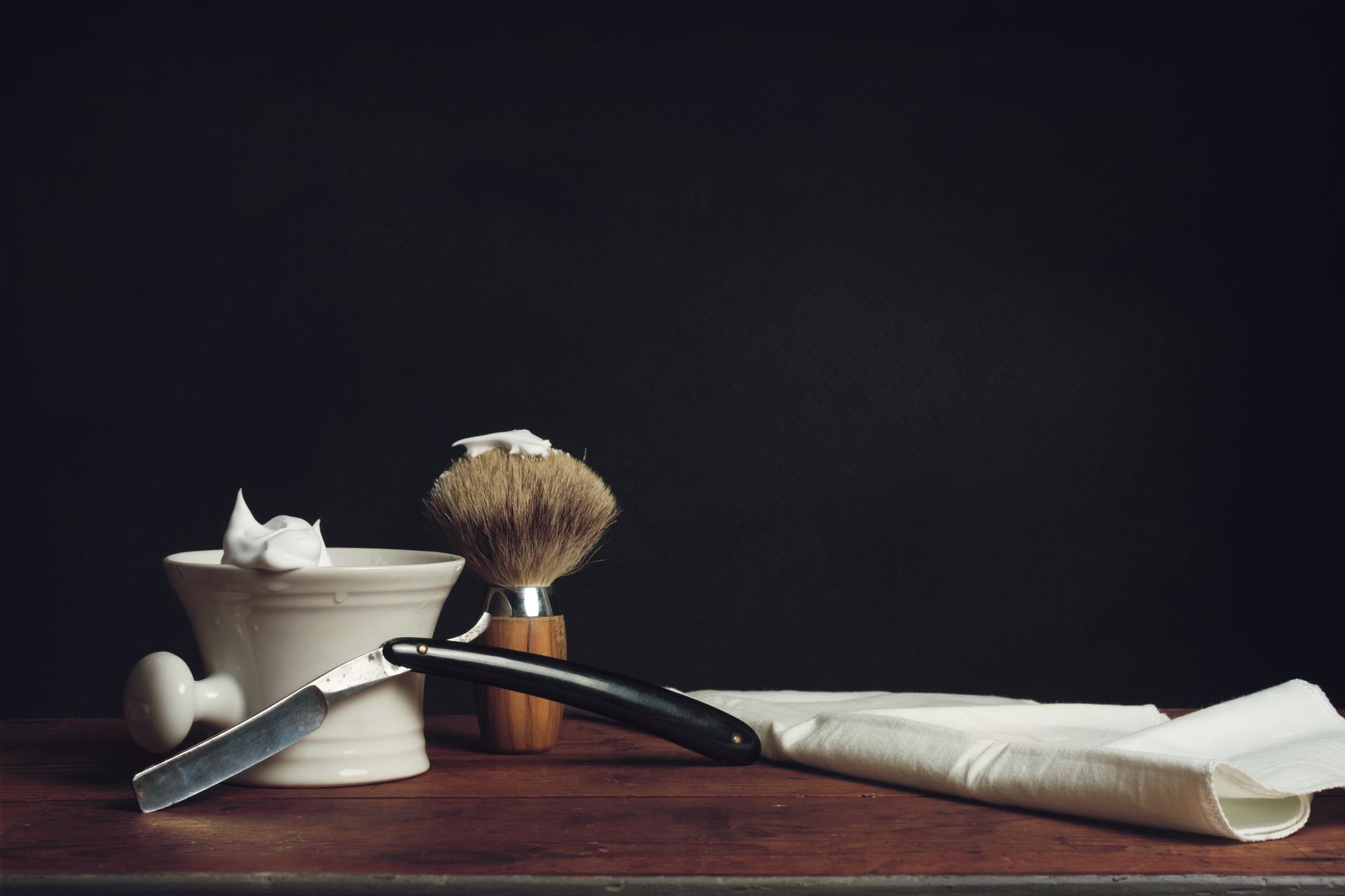 A shaving brush , razor , and soap are on a wooden table.