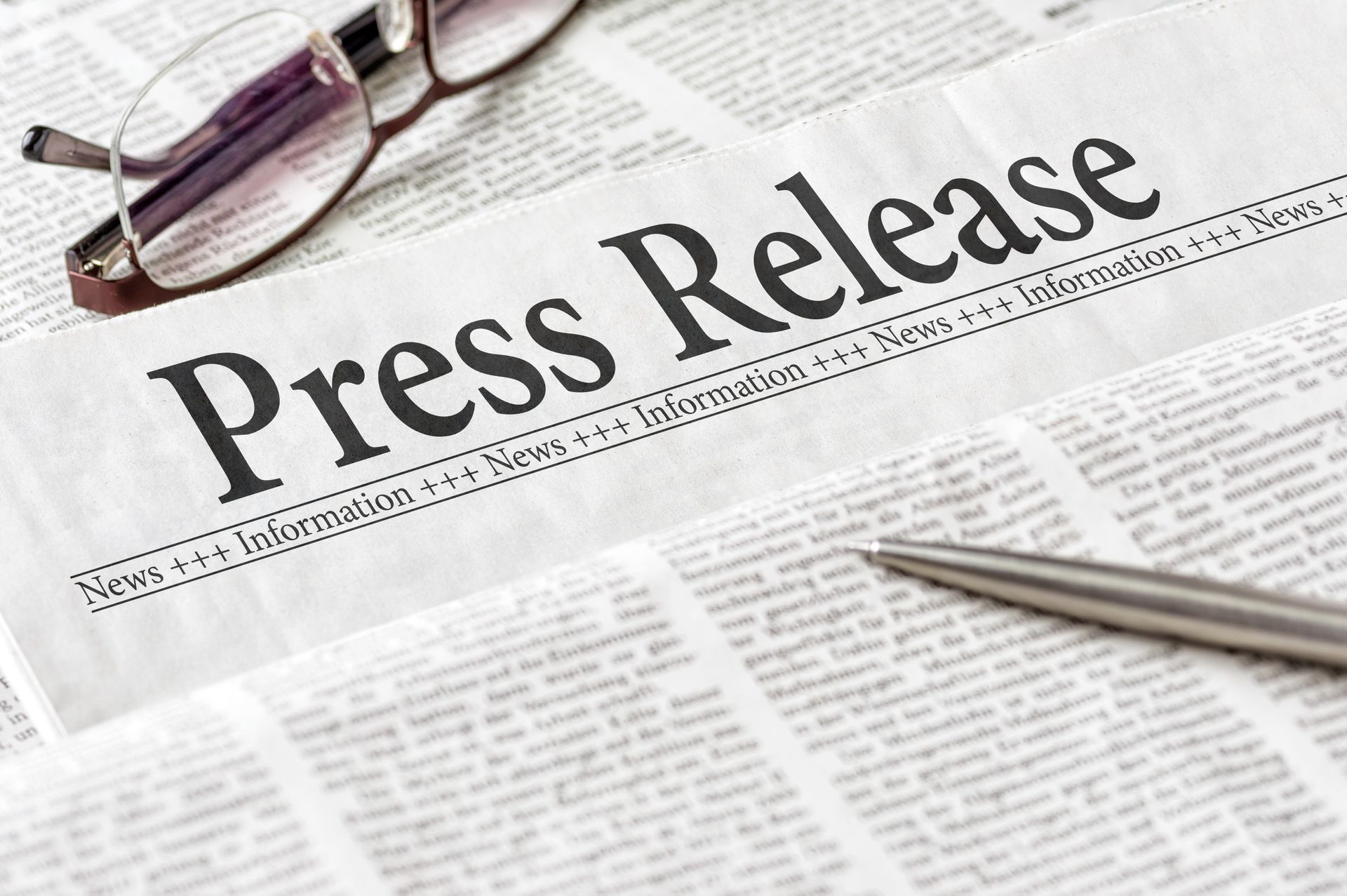 A pair of glasses and a pen are sitting on top of a newspaper that says press release.