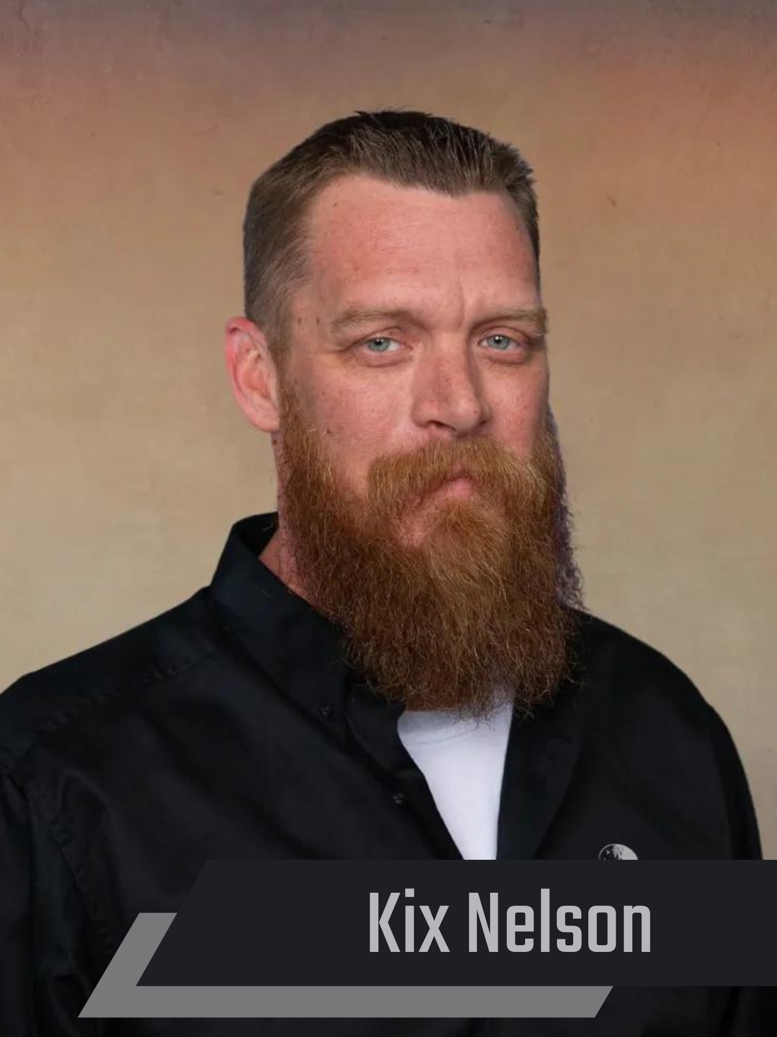 Kix Nelson, a man with a red beard, wears a black shirt, and stares forward.