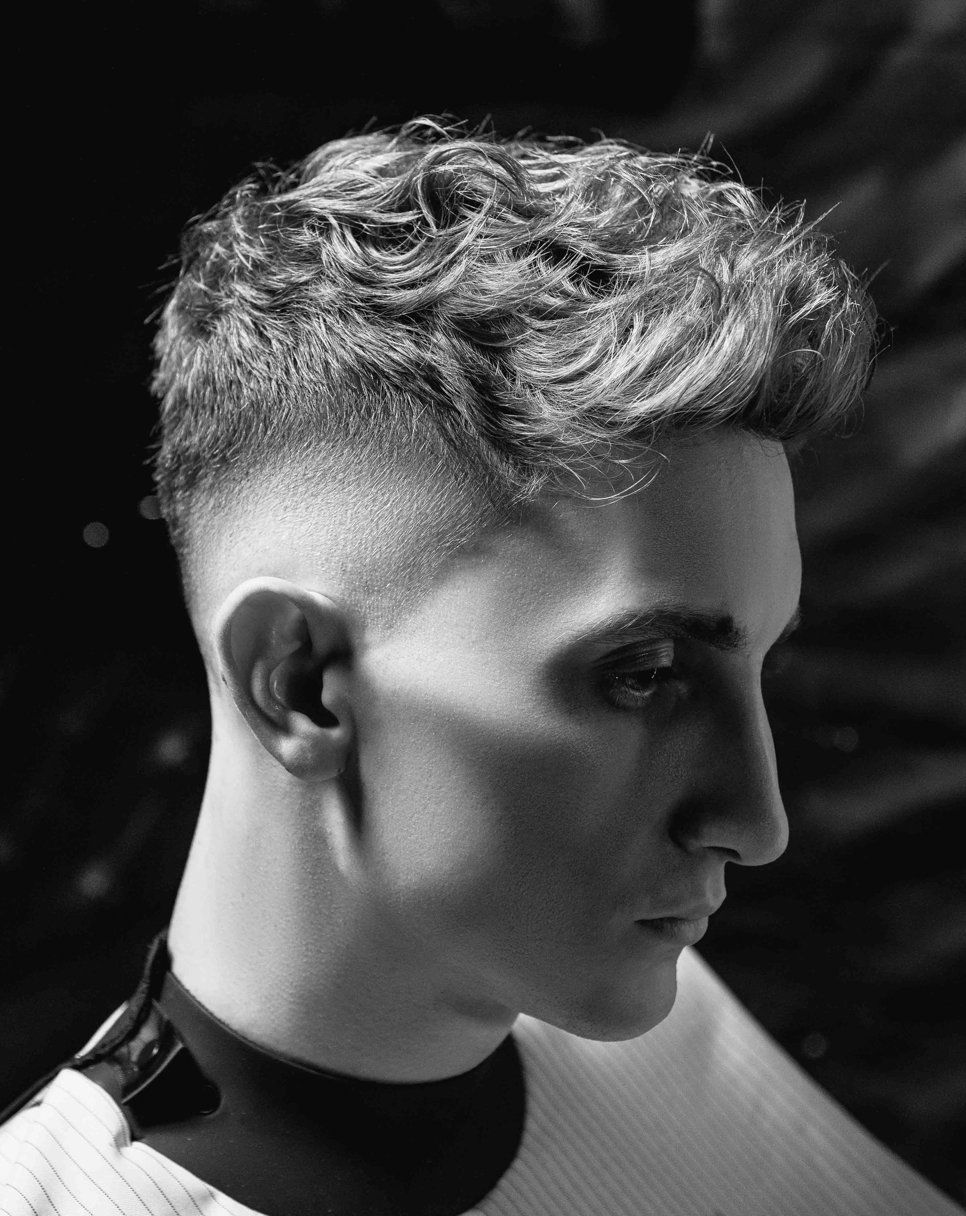 A man with curly hair is getting his hair cut by a barber in a black and white photo.