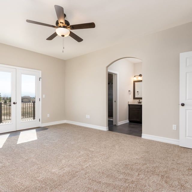 An empty room with a ceiling fan and sliding glass doors