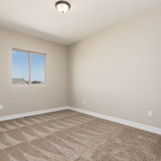 An empty bedroom with a carpeted floor and a window.