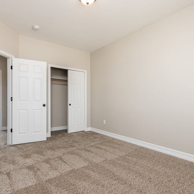 An empty bedroom with a carpeted floor and white doors