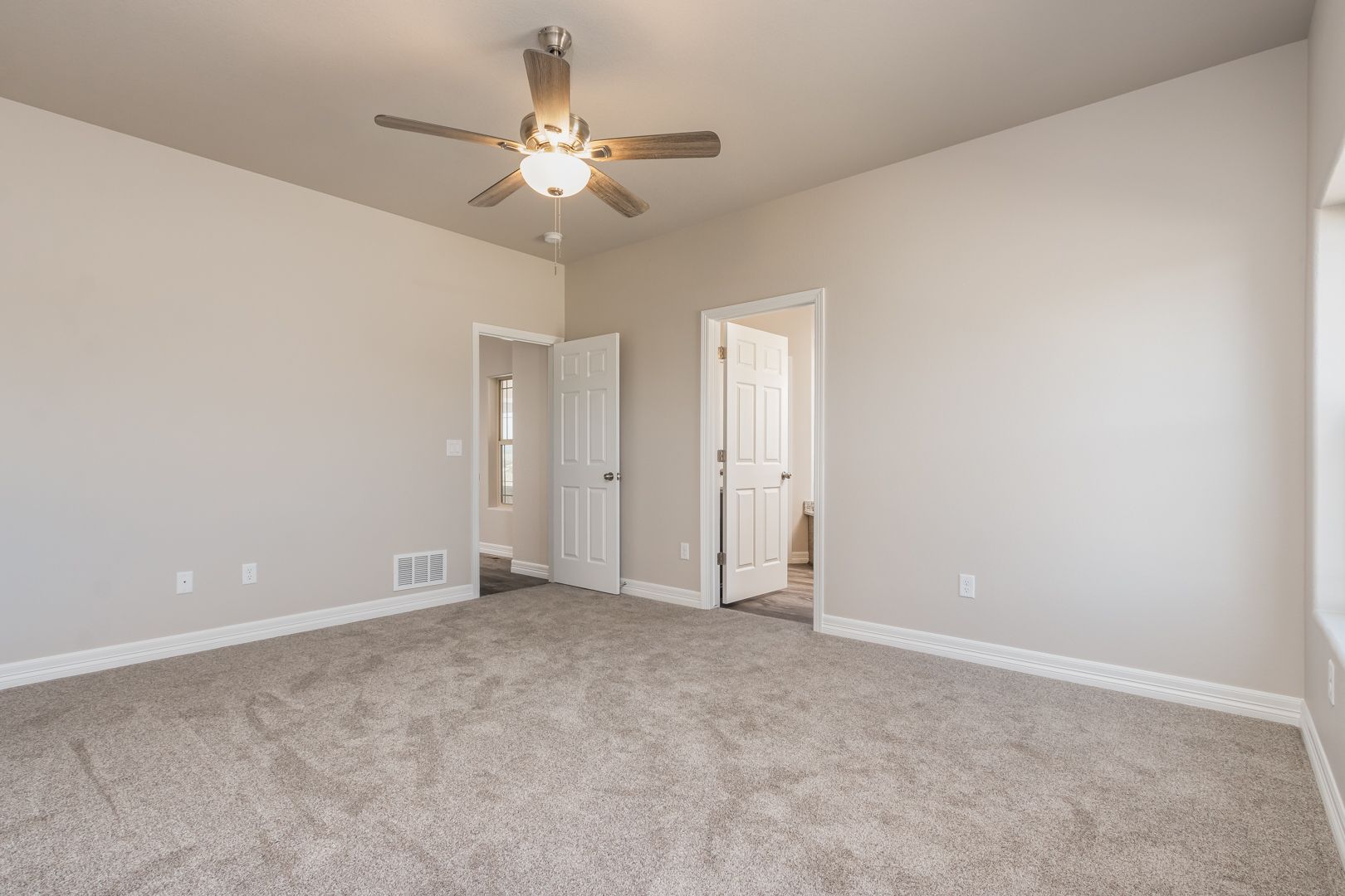 An empty bedroom with a ceiling fan and a carpeted floor.