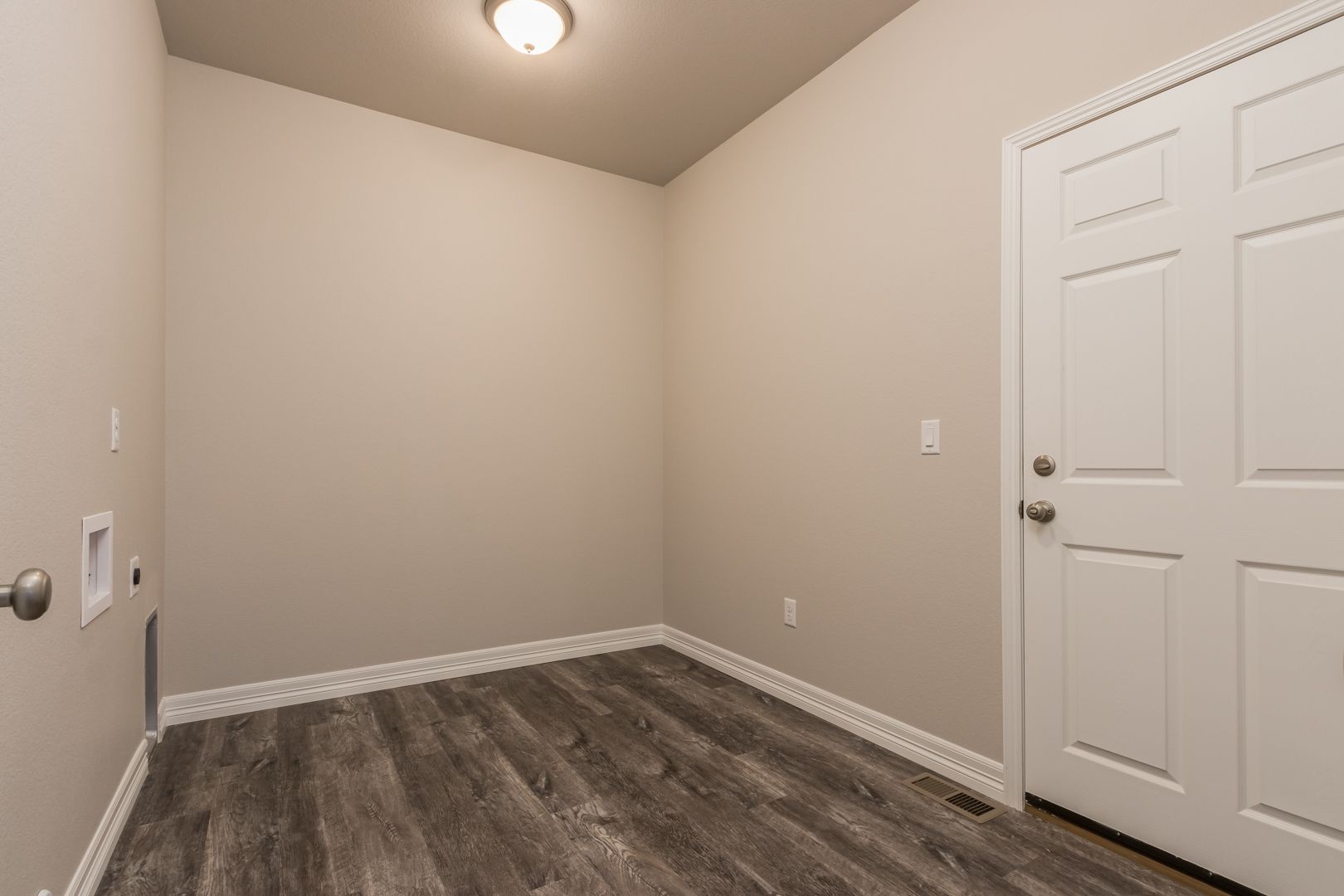 An empty laundry room with hardwood floors and a door.