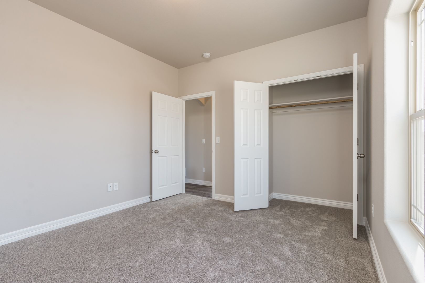 An empty bedroom with a closet and a window.