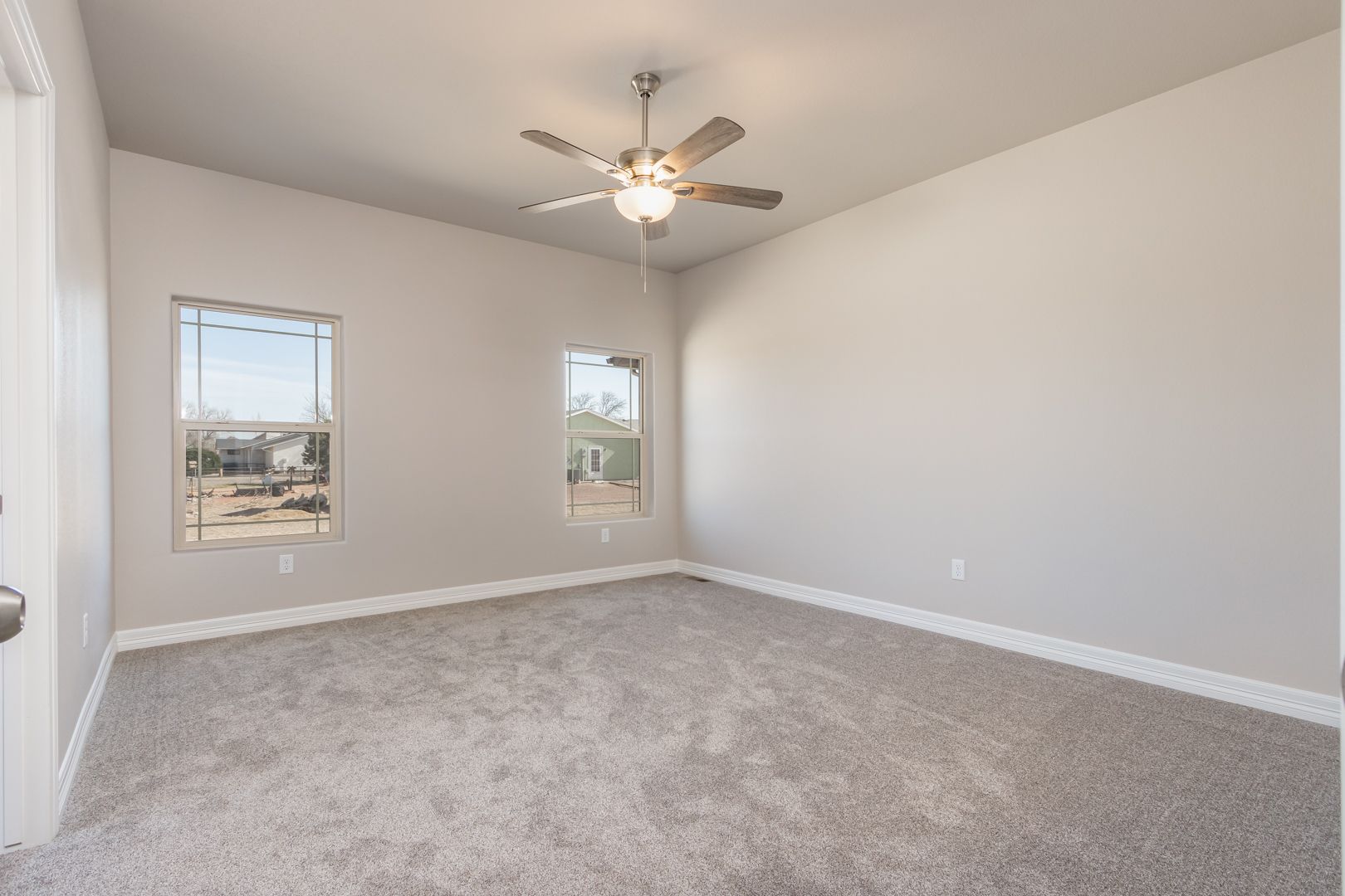 An empty bedroom with a ceiling fan and two windows.