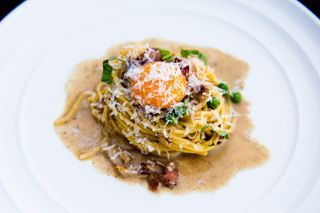 Pasta with meat sauce, basil, and grated cheese in a white bowl
