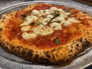 Pepperoni pizza topped with onion rings on a floured surface, with tomatoes, garlic, and eggs nearby