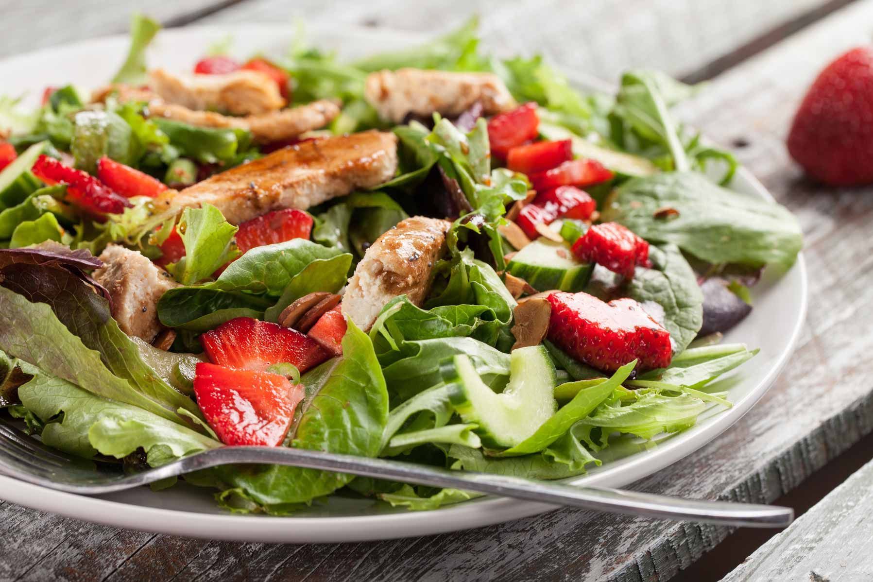 Fresh salad with strawberries, greens, and toasted bread on a white plate