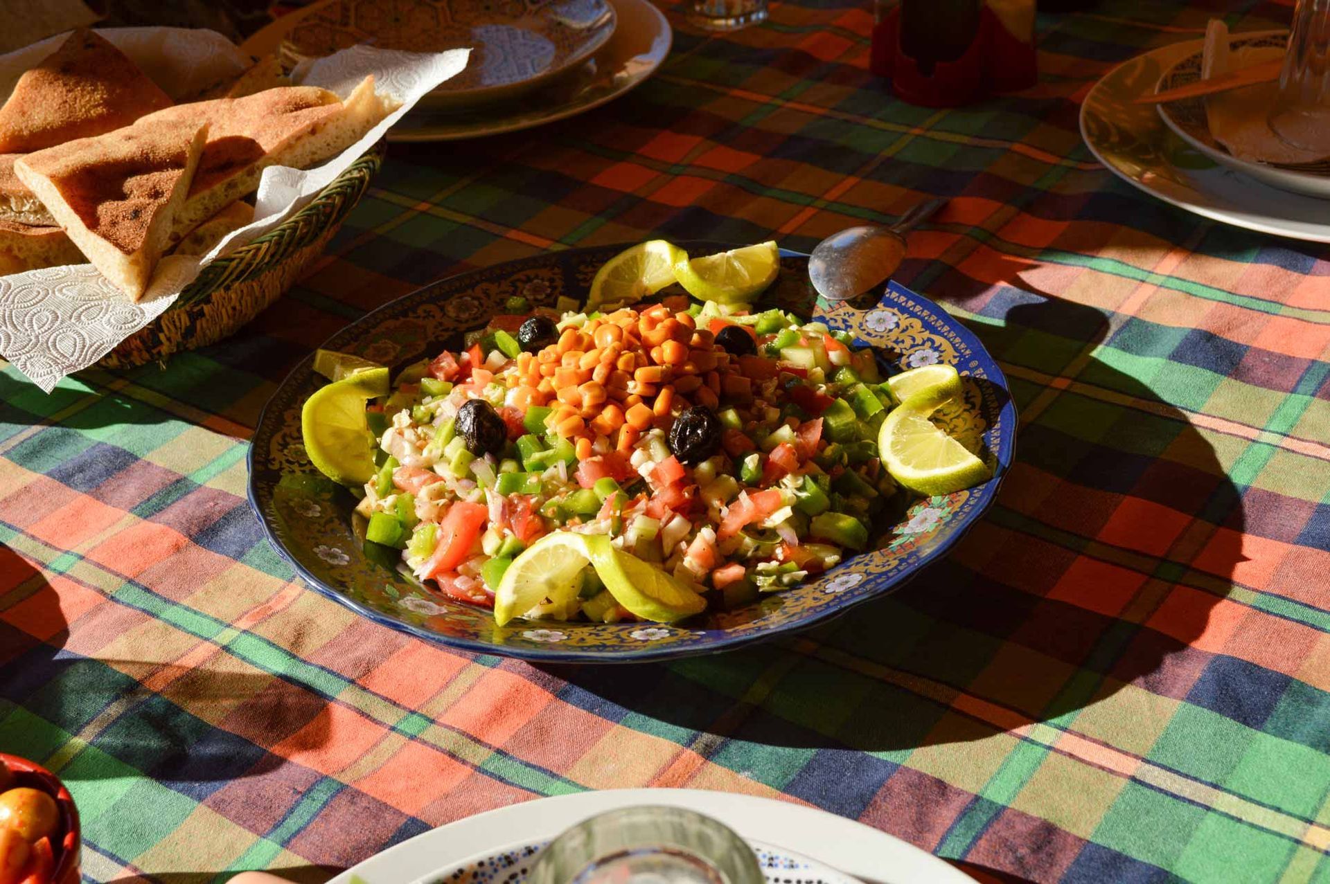 Platter of seasoned salad with lime wedges on a plaid tablecloth, with bread on the side