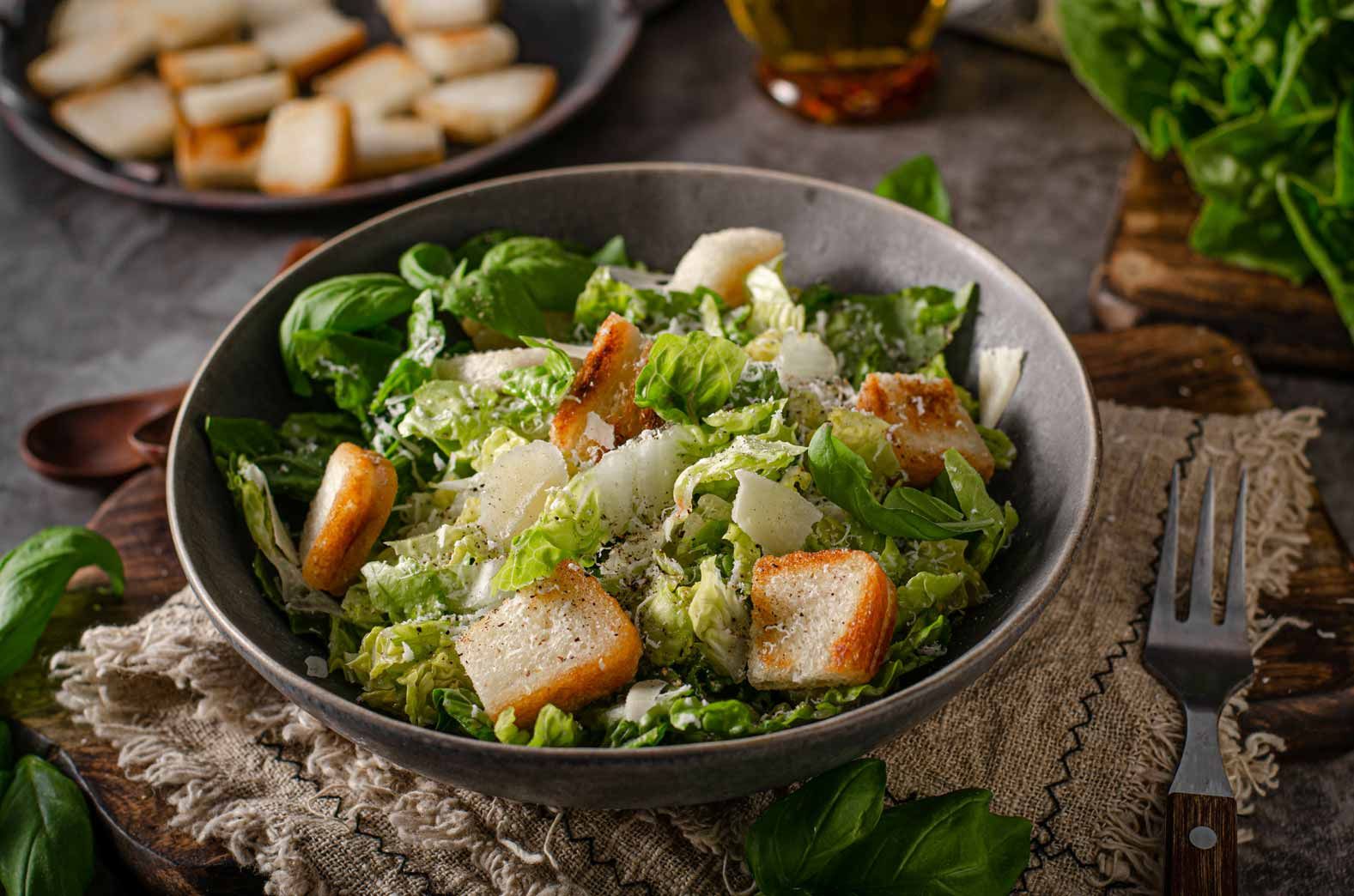 Caesar salad in a black bowl with croutons, lettuce, and parmesan on a rustic table