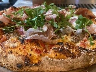Baked pizza with melted cheese, broccoli, onions, and olives on a plate with a fork