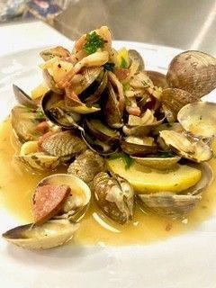 Bowl of cooked clams in a reddish pot on a dining table with blurred dishes in the background