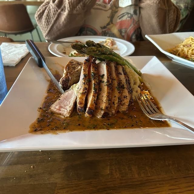 Plated sliced grilled meat with asparagus and sauce on a white square plate in a restaurant