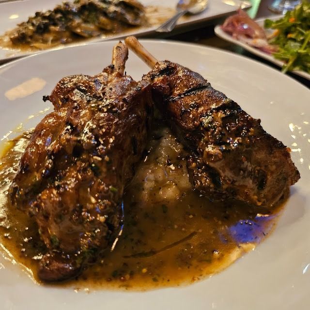 Grilled meat chops in brown sauce on a white plate with herbs in the background