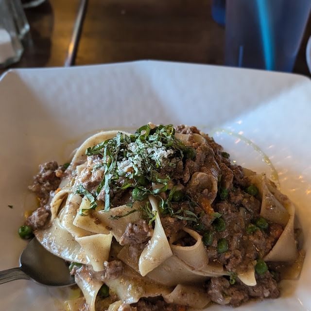 Pasta with meat sauce and herbs on a white plate in a restaurant setting