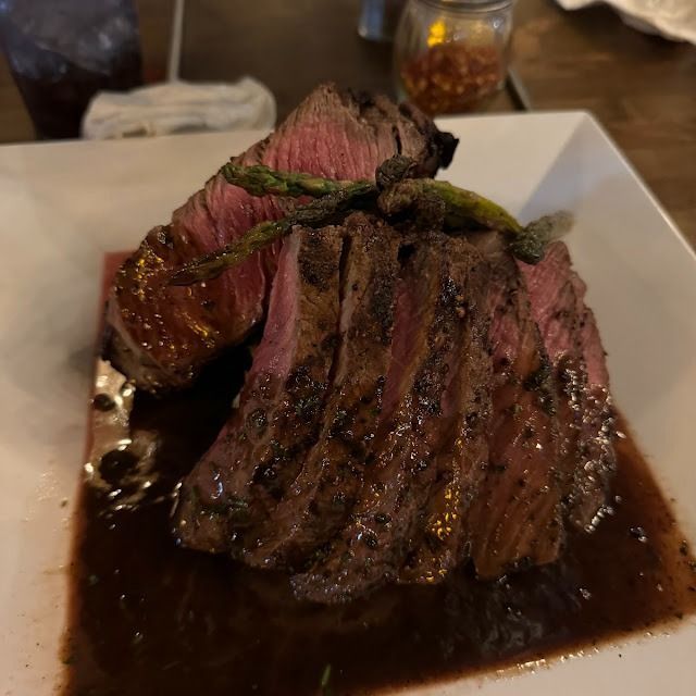 Seared steak on a white plate, sliced to show a pink center and covered in dark sauce.