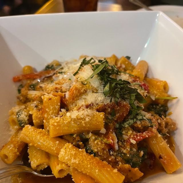 Penne pasta in a white bowl, topped with grated cheese, herbs, and tomato sauce