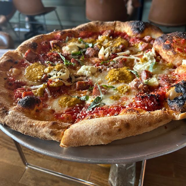 Wood-fired pizza on a plate, topped with melted cheese, herbs, and dollops of sauce in a restaurant setting